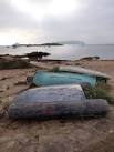 Several small boats and inflatables lie upturned on the seafront near the - via Daymix