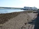Stony beach with a garish paint job of a cruise liner beyond (Aida Luna). - via Daymix