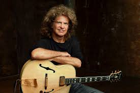 White man leaning on semi-acoustic guitar.